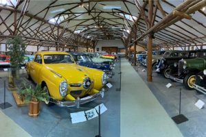 Autos antiguos en fila dentro del Museo Autos Moncopulli, con un auto amarillo en primer plano y estructura de madera visible